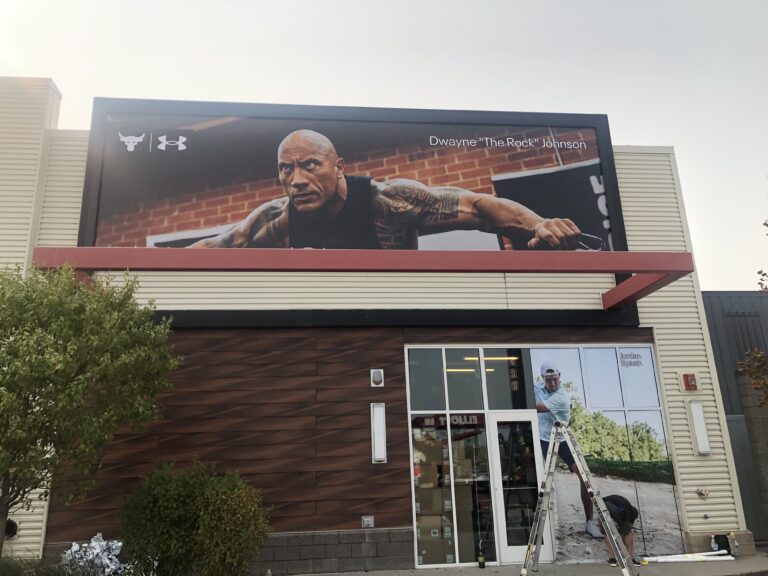 D8 Sign Group employee installing window wrap design of golfer at the Under Armour store